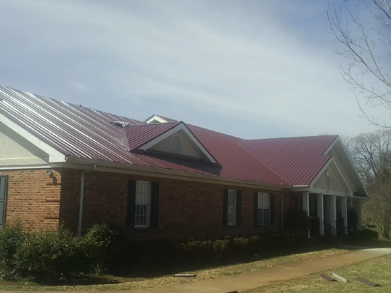Red metal roof with gabled entries on a long brick building, from a Hail Damage Roof Repair job in Holbrook