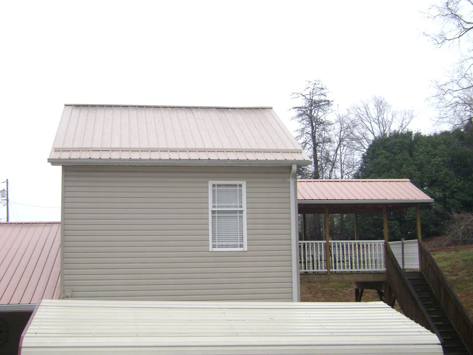 Tan metal roofs on a two story addition and attached porch, from a Roof Replacement job in Holbrook